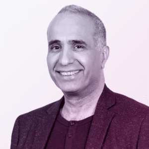 A middle-aged man with short gray hair, smiling, wearing a blazer over a dark shirt, posed against a light background.